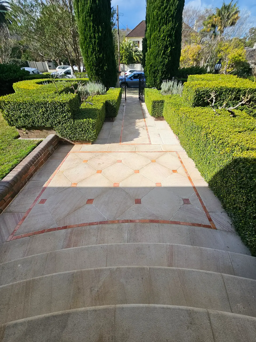 Formal sandstone entry forecourt with terracotta brick banding and a geometric diamond inlay